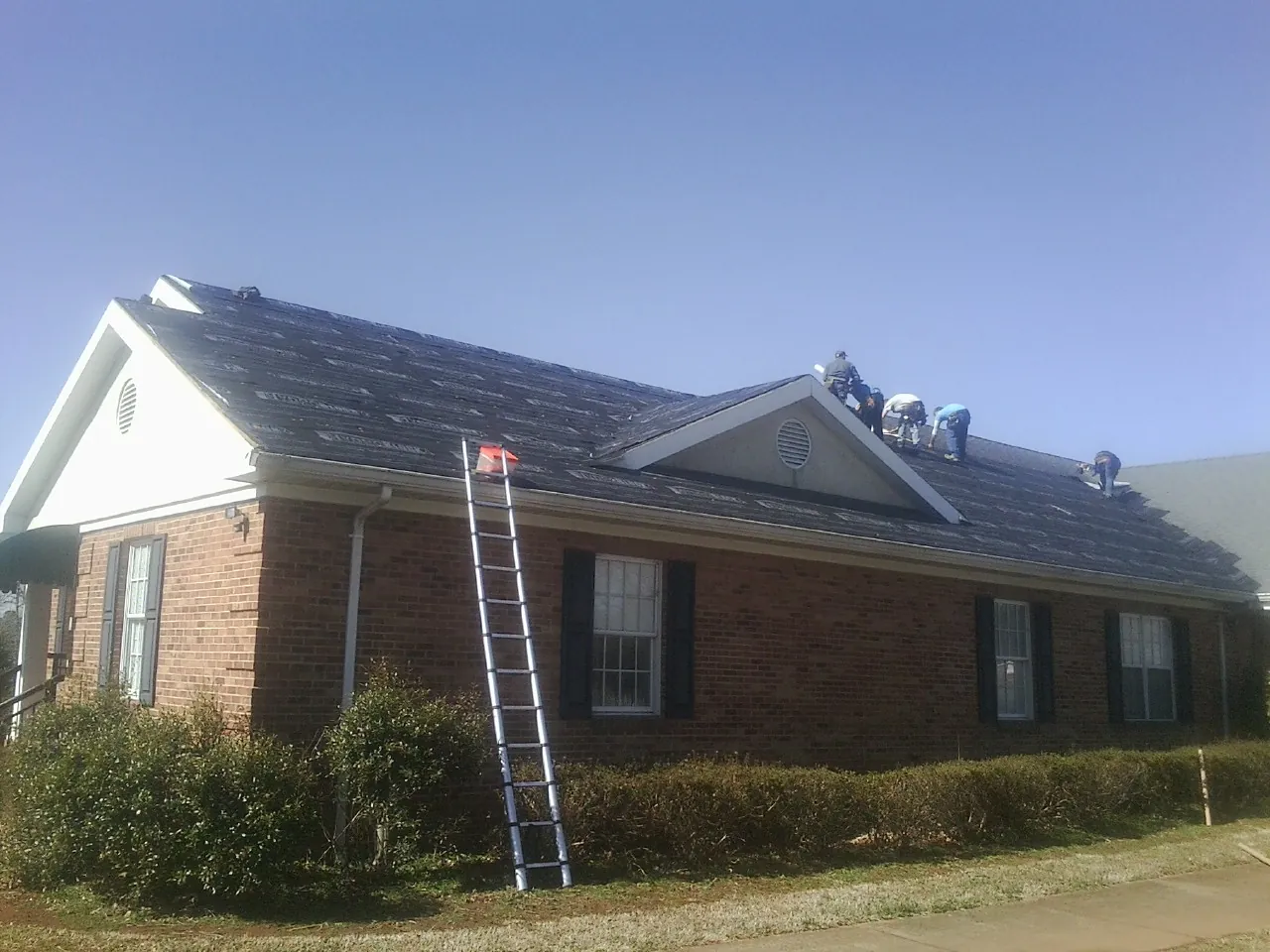 Crew tearing shingles off a brick ranch roof with a ladder set — Metal Roof Repair work by our crew in Mechanic Falls