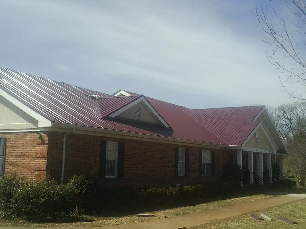 Red metal roof with gabled entries on a long brick building, from a Hail Damage Roof Repair job in Mechanic Falls