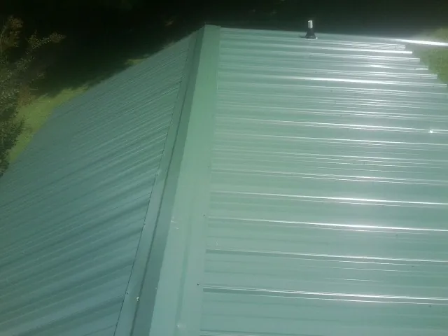 New green metal panels meeting at the ridge of a roof — Flat Roof Repair work by our crew in Mechanic Falls