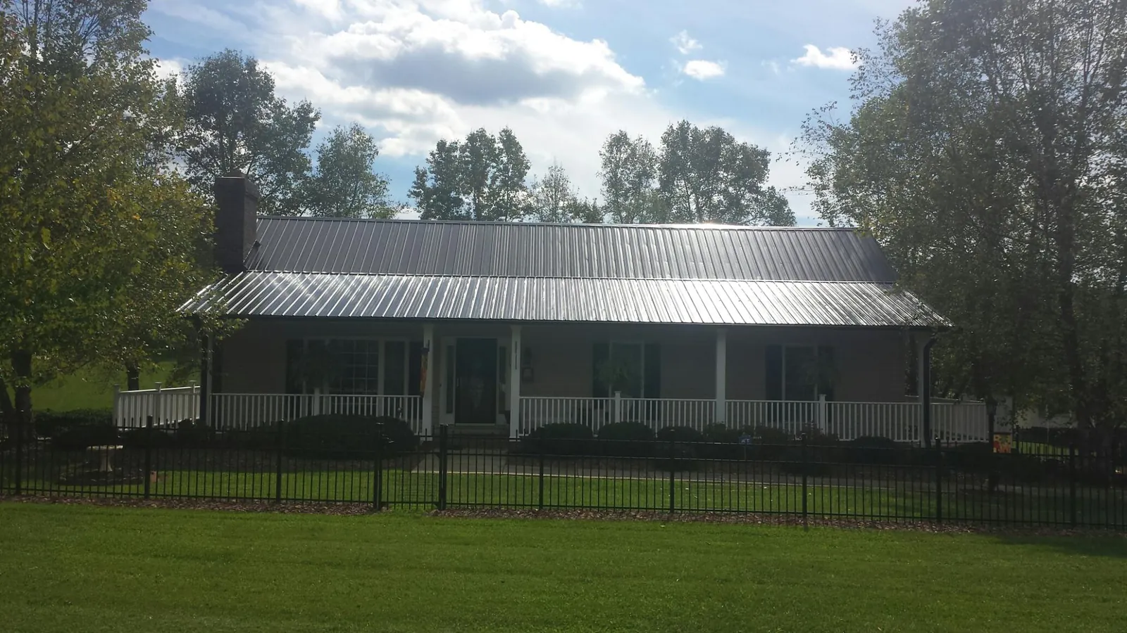 Gray metal roof on a brick ranch with a full width front porch — Gutter Guard Installation work by our crew in Mechanic Falls
