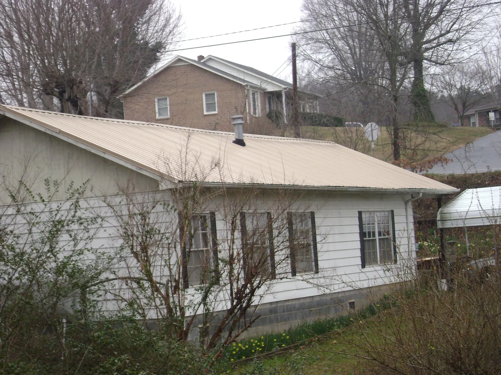 Tan metal roof on a white sided house set into a hillside — Commercial Roofing by Roofing Brothers in Mechanic Falls