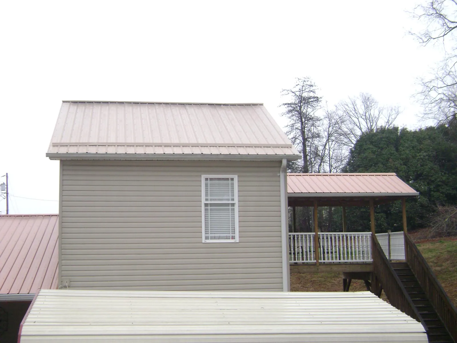 Tan metal roofs on a two story addition and attached porch, from a Roof Replacement job in Mechanic Falls